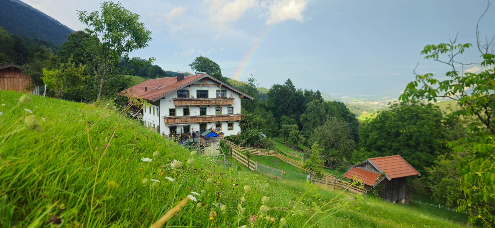 Wohnhaus des Kruckenhaus am Hang mit Regenbogen über dem Tal im Sommer